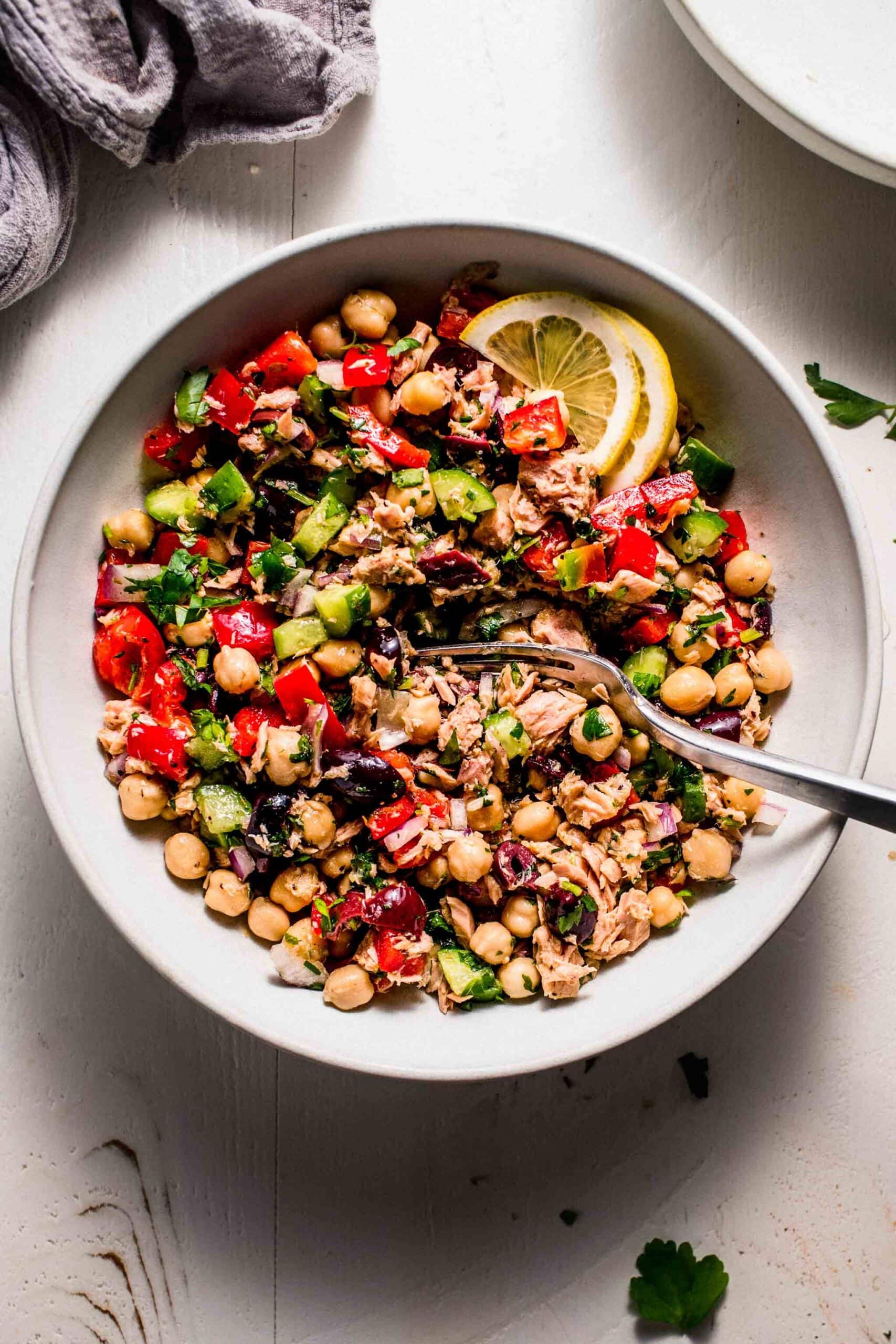 Tuna chickpea salad in bowl with lemon wedges and serving spoon.