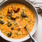 Overhead shot of broccoli cheese soup in white bowl with spoon.