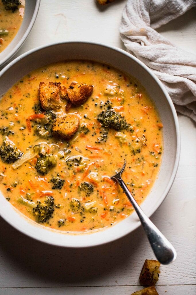 Overhead shot of instant pot broccoli cheese soup in white bowl with spoon.