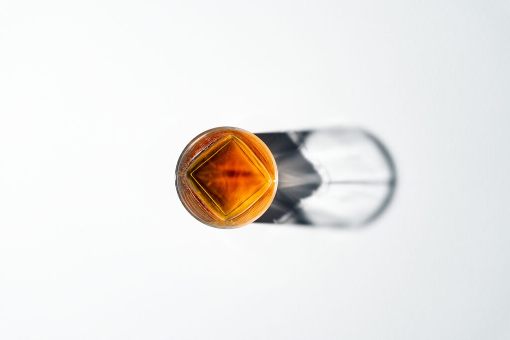 Glass of whiskey with large cube on white counter. 