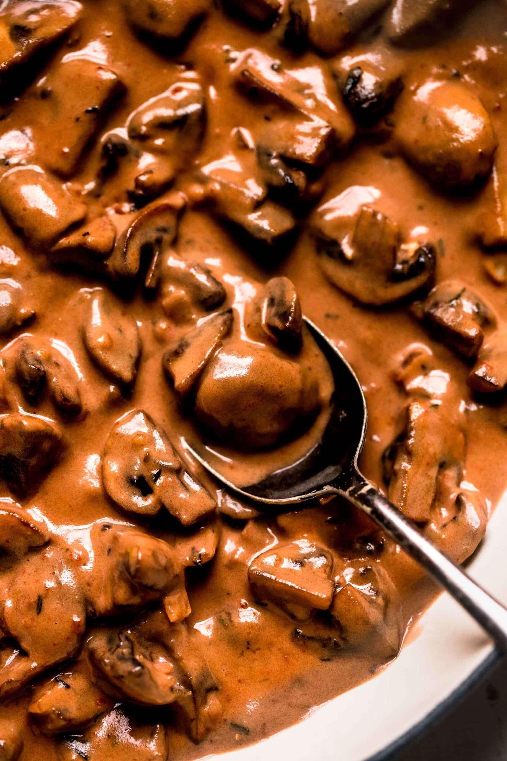 Overhead closeup of creamy mushroom sauce in skillet with spoon.