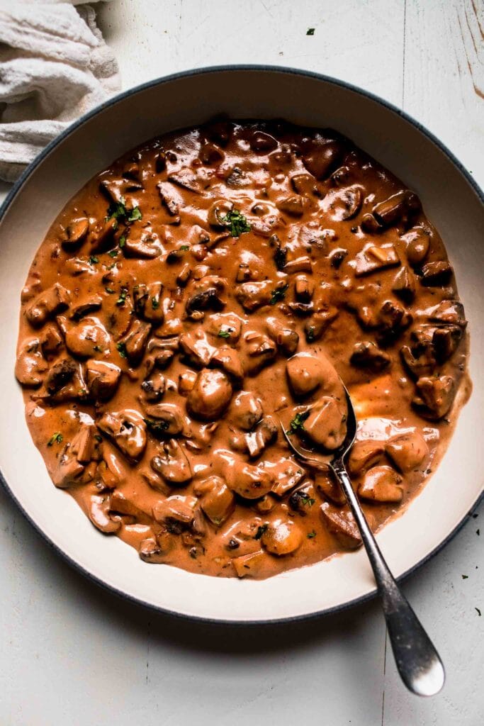 Mushroom sauce in white skillet with spoon.