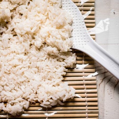 Sushi rice laid out on rolling mat with rice paddle.