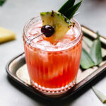 Prepared tiki cocktail garnished with pineapple leaves and cherry.