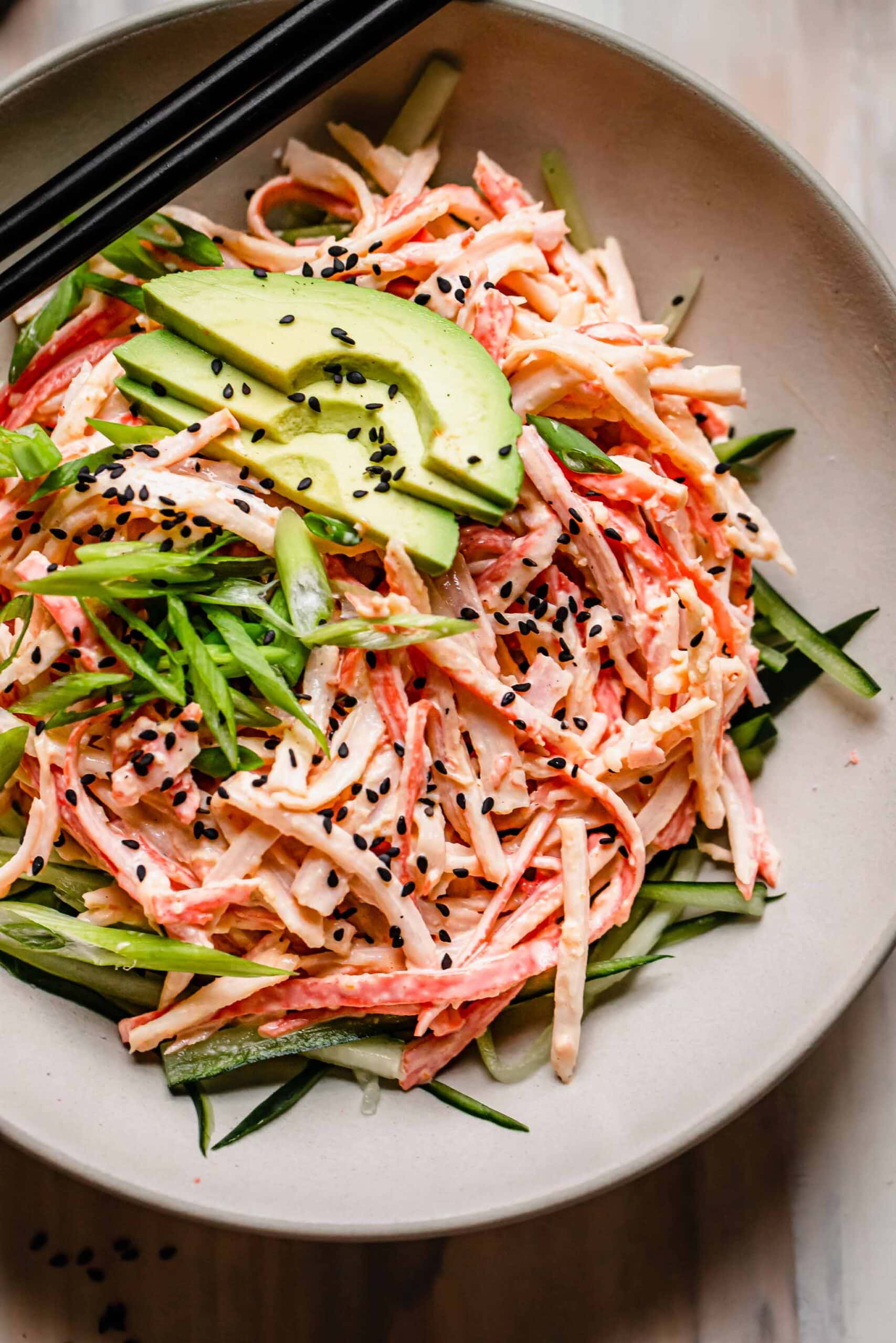 Overhead shot of kani salad in bowl topped with avocado and sesame seeds.