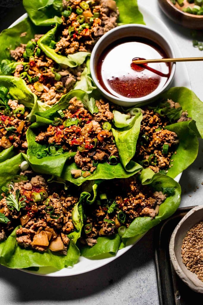 Lettuce wraps arranged on plate with dipping sauce in bowl. 