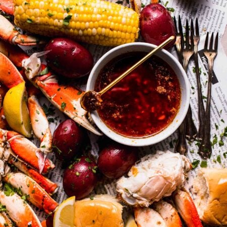 Bowl of seafood boil sauce with spoon next to seafood boil spread on newspapers.