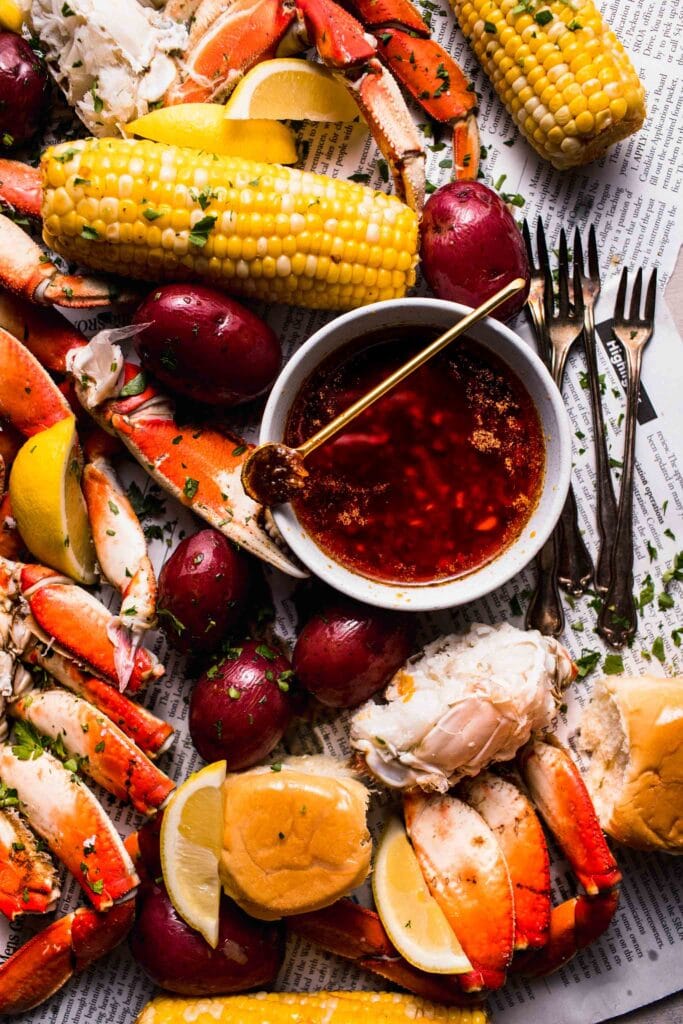 Bowl of seafood boil sauce with spoon next to seafood boil spread on newspapers.