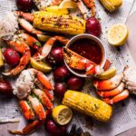 Seafood boil spread out on newspapers with small bowl of garlic butter sauce.
