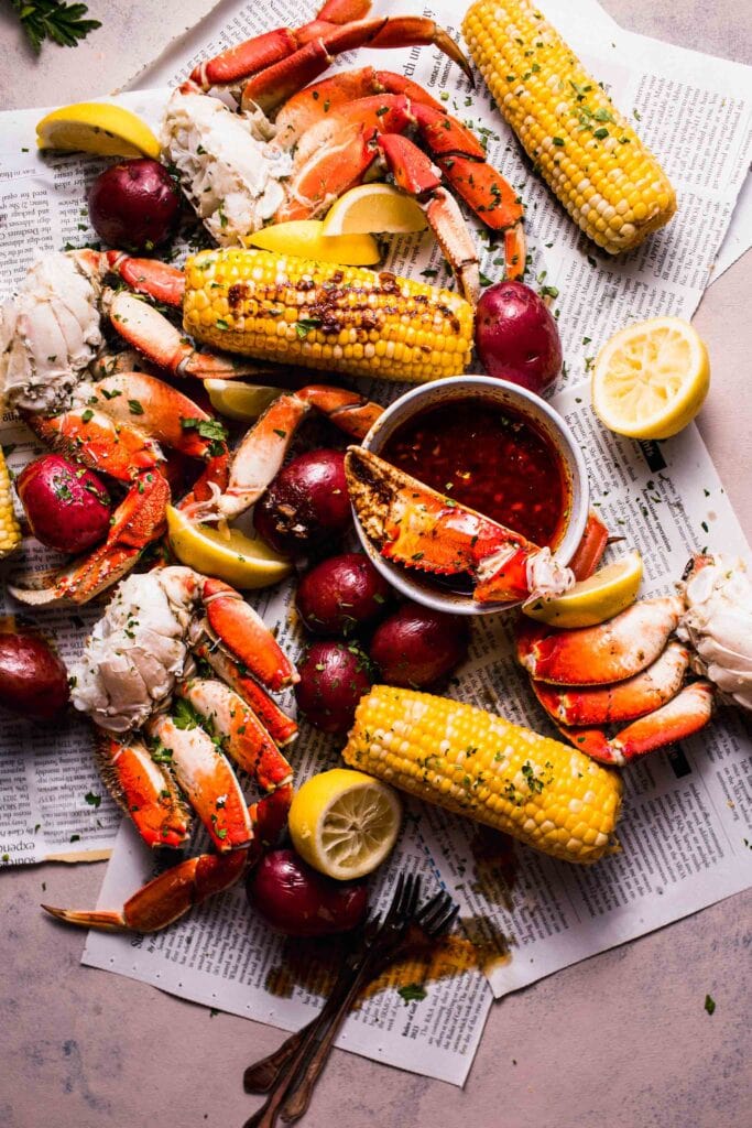 Seafood boil spread out on newspapers with small bowl of garlic butter sauce.