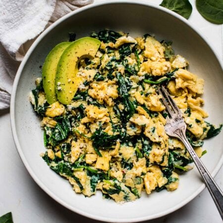 Overhead shot of spinach scrambled eggs in white bowl with fork.