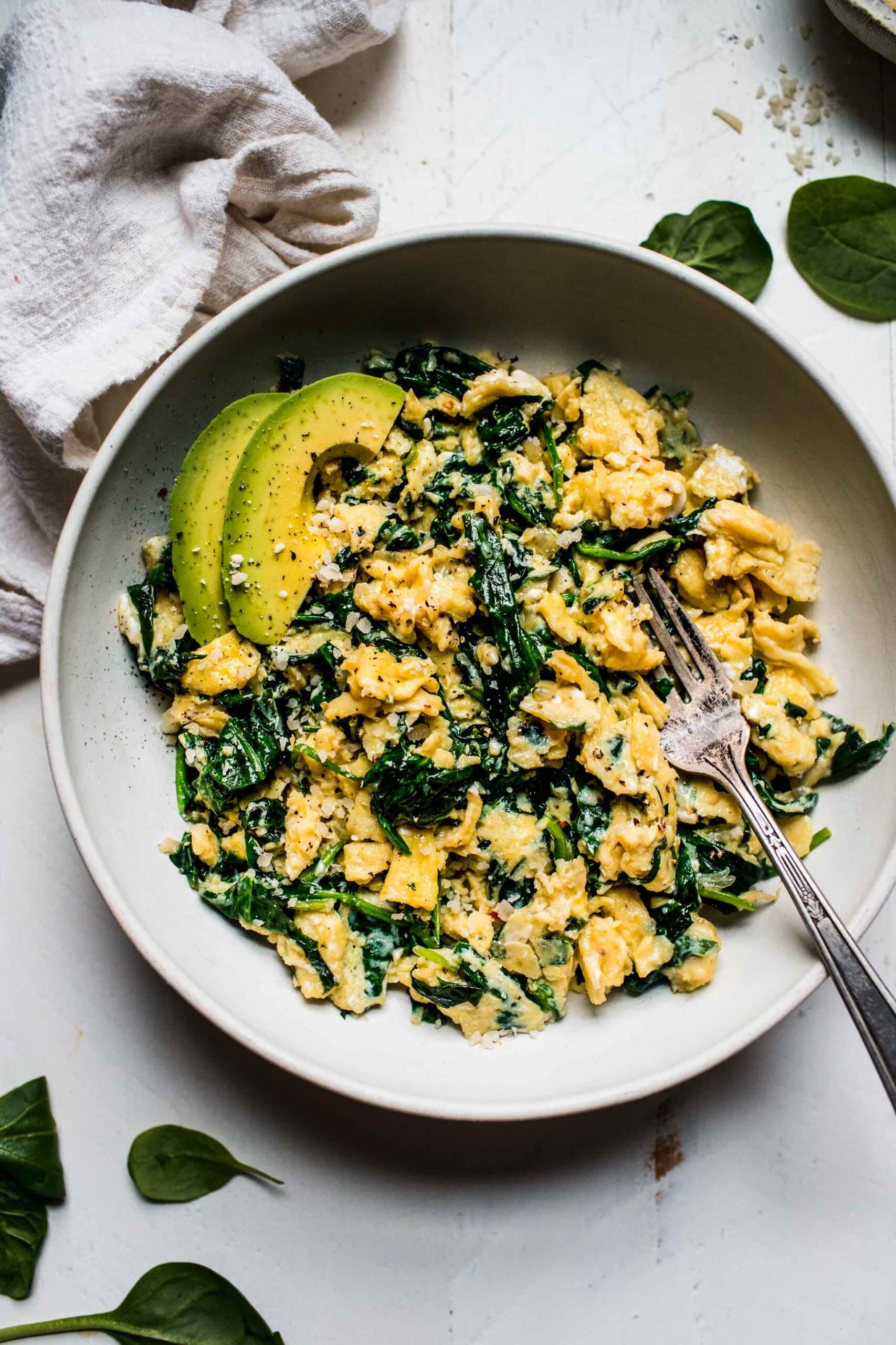 Overhead shot of spinach scrambled eggs in white bowl with fork.