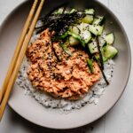 Spicy tuna layered over bowl of rice with nori and cucumbers.