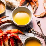 Small bowl of crab butter next to cracked crabs on newspapers.