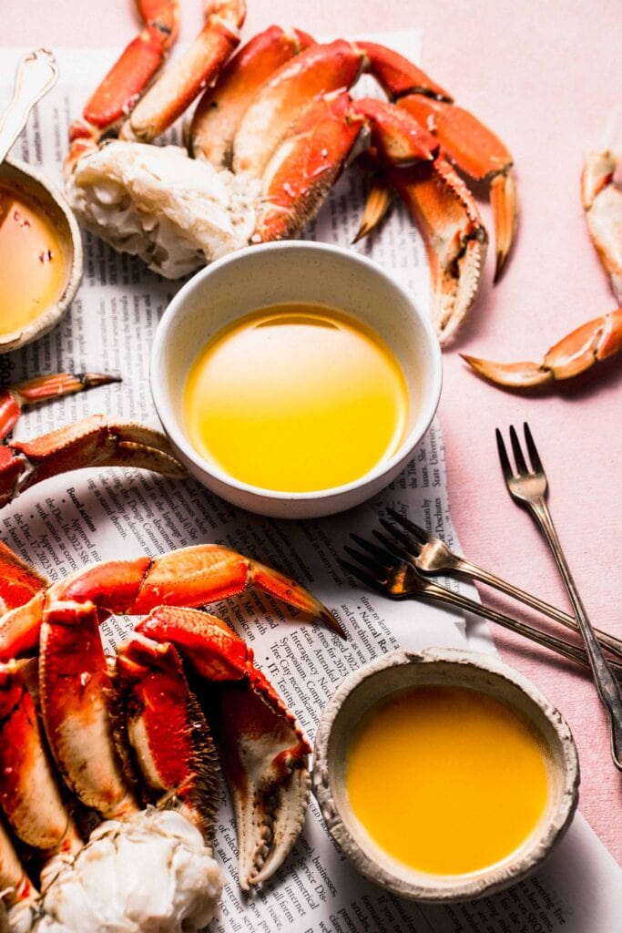 Small bowl of crab butter next to cracked crabs on newspapers.