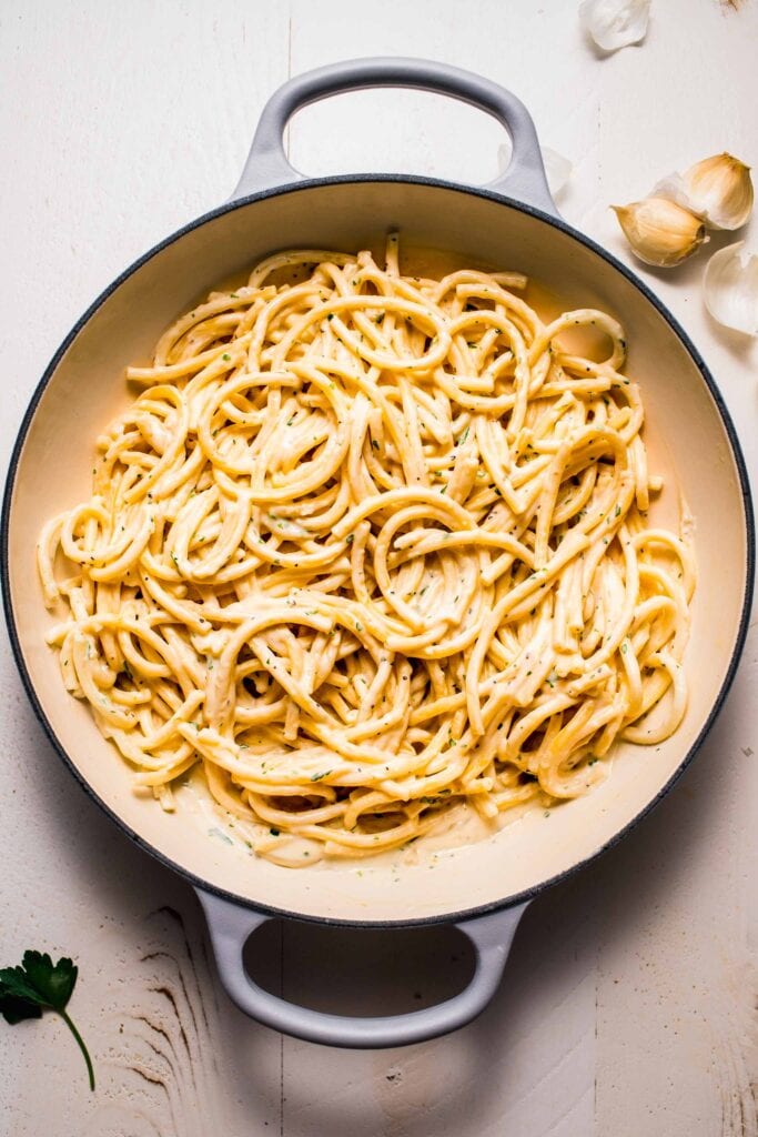 Pasta tossed with creamy garlic sauce in skillet. 