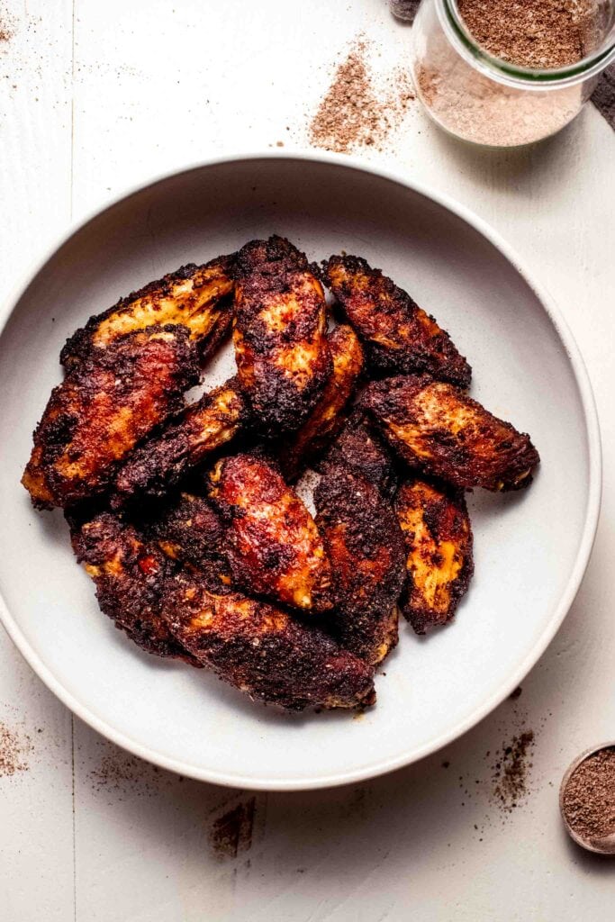 Chicken wings in white bowl next to small jar of wing dry rub.