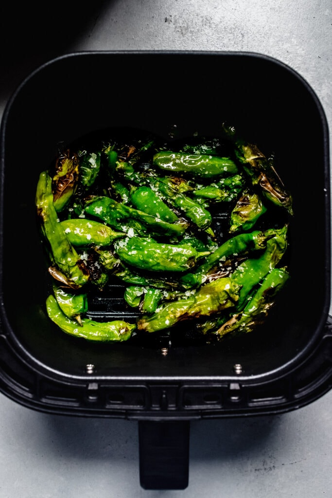 Blistered shishito peppers in air fryer basket.