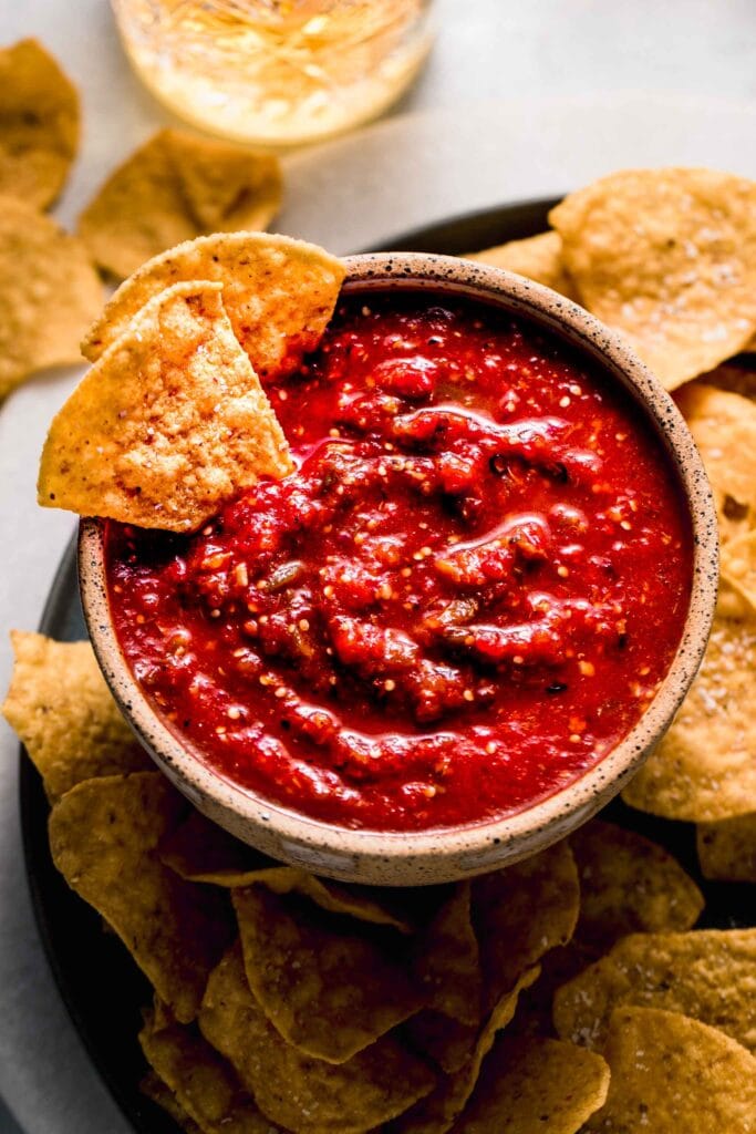 Bowl of chipotle salsa on plate with chips scattered about. 