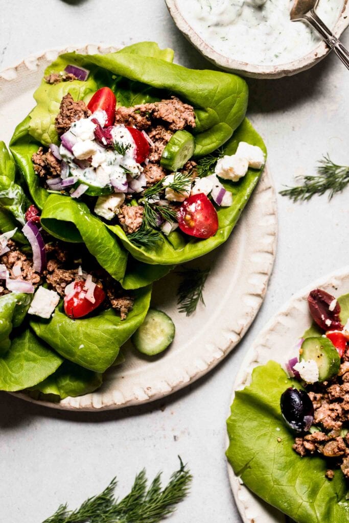 Lamb wraps on small plate next to bowl of tazatziki. 