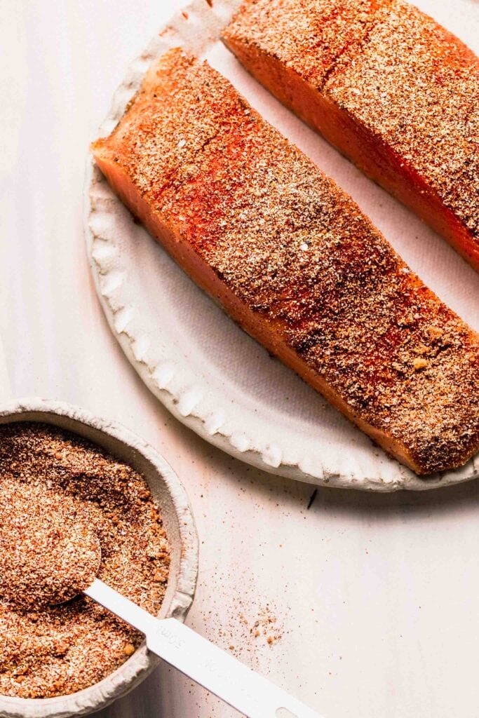 Two uncooked salmon filets coated in dry rub.