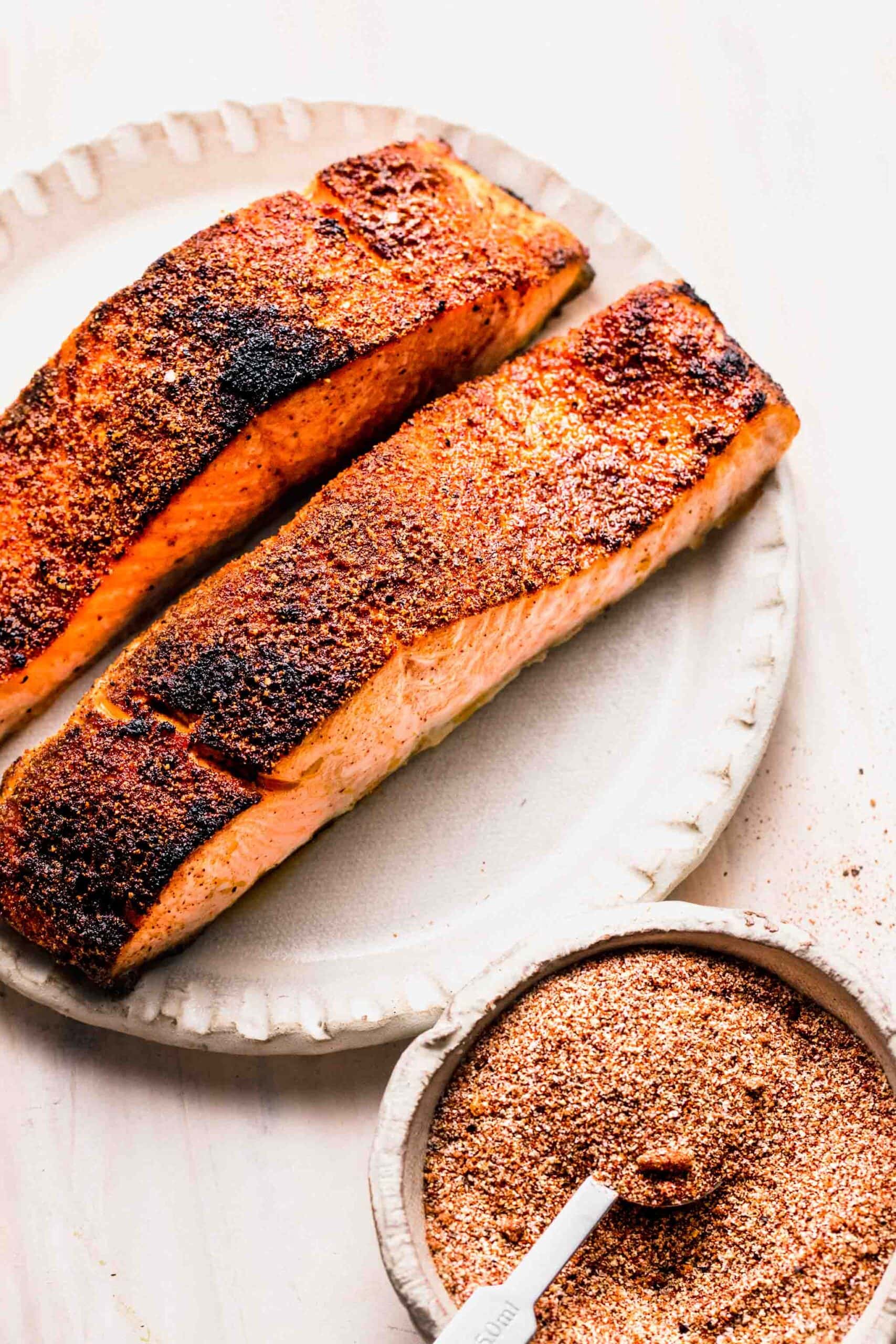 Two cooked filets of salmon next to small bowl of salmon dry rub.