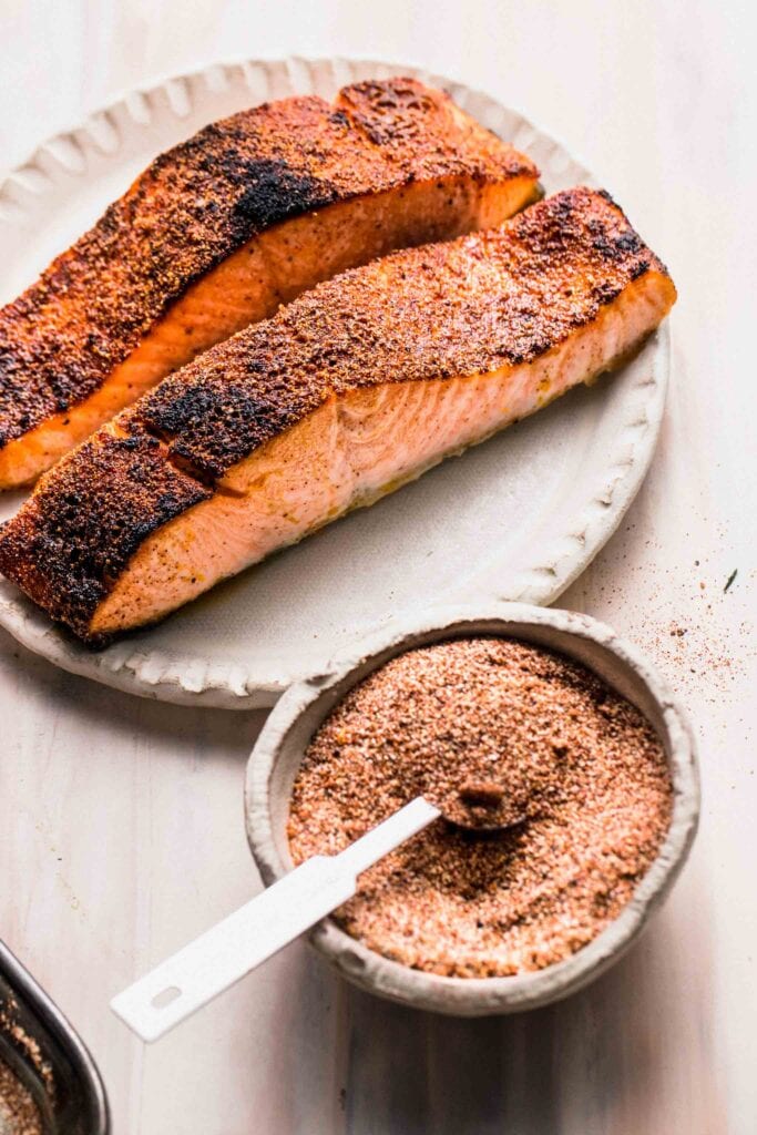 Two seared salmon filets on plate next to bowl of salmon dry rub.