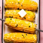 Ears of corn on serving plate with pat of butter.