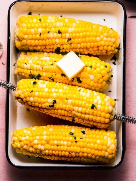 Ears of corn on serving plate with pat of butter.