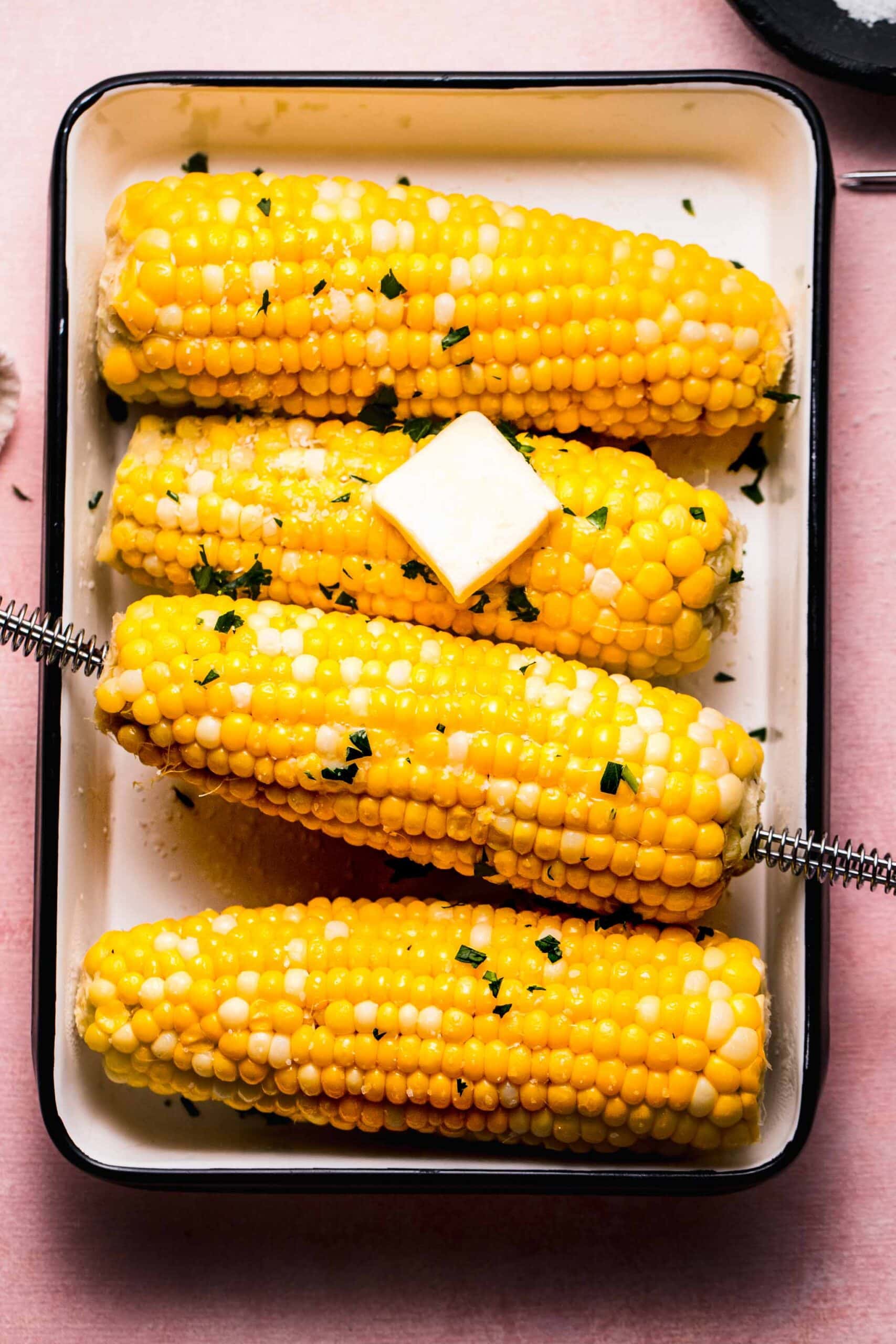 Ears of corn on serving plate with pat of butter.