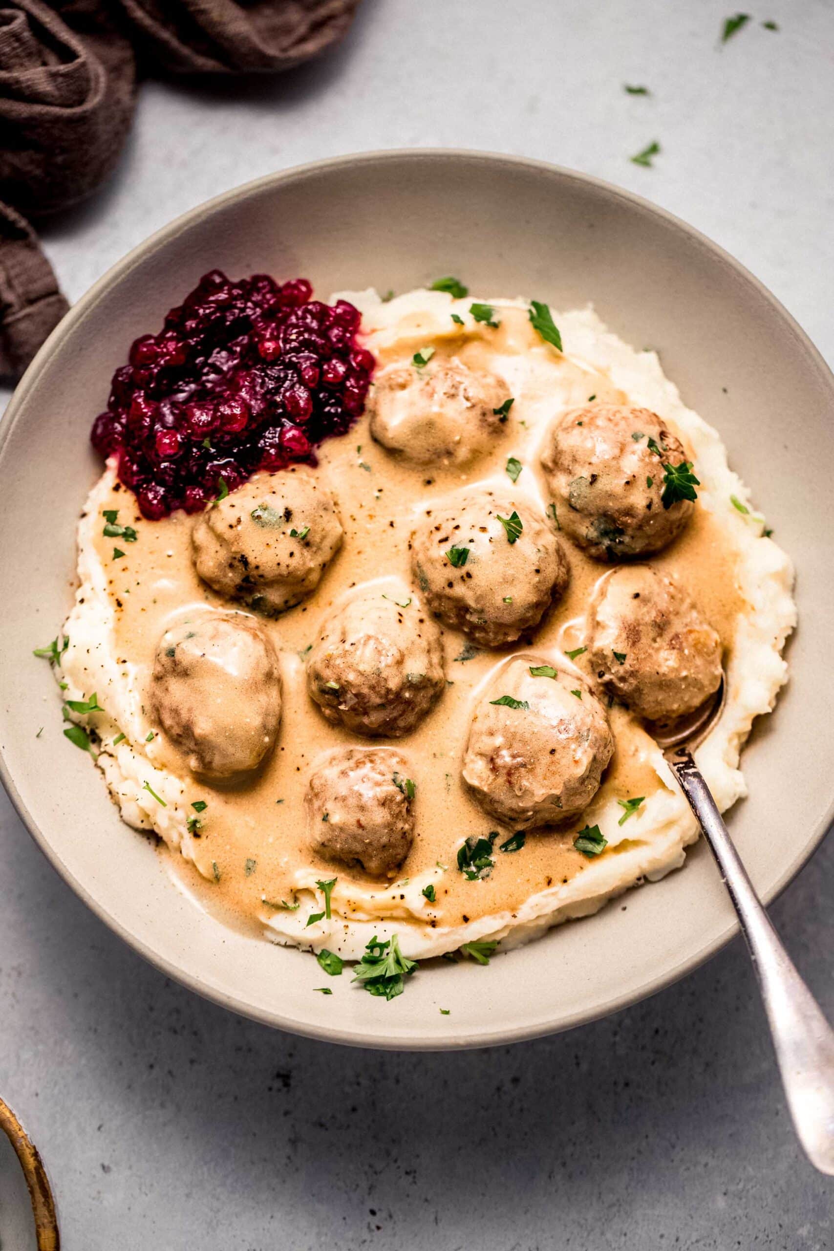 Turkey swedish meatballs arranged in bowl with mashed potatoes and dollop of lingonberry jam.