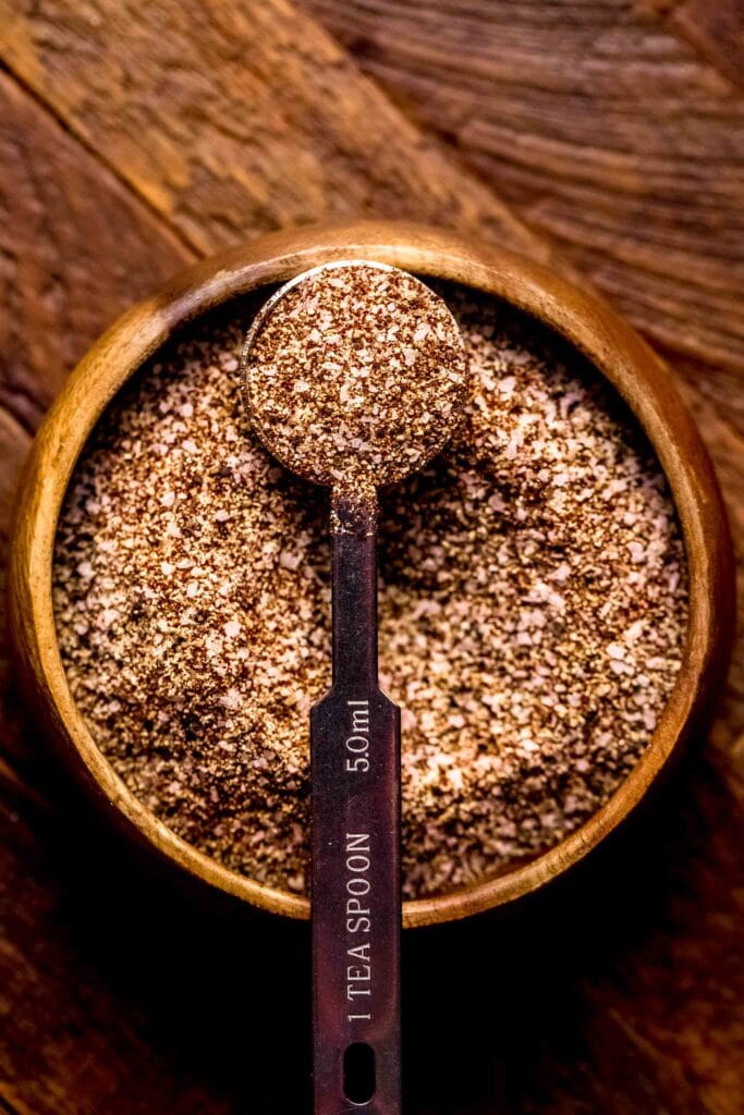 Brisket dry rub in small wooden bowl with teaspoon.