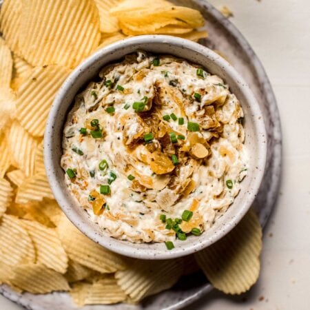 Overhead shot of greek yogurt onion dip in bowl surrounded by potato chips.