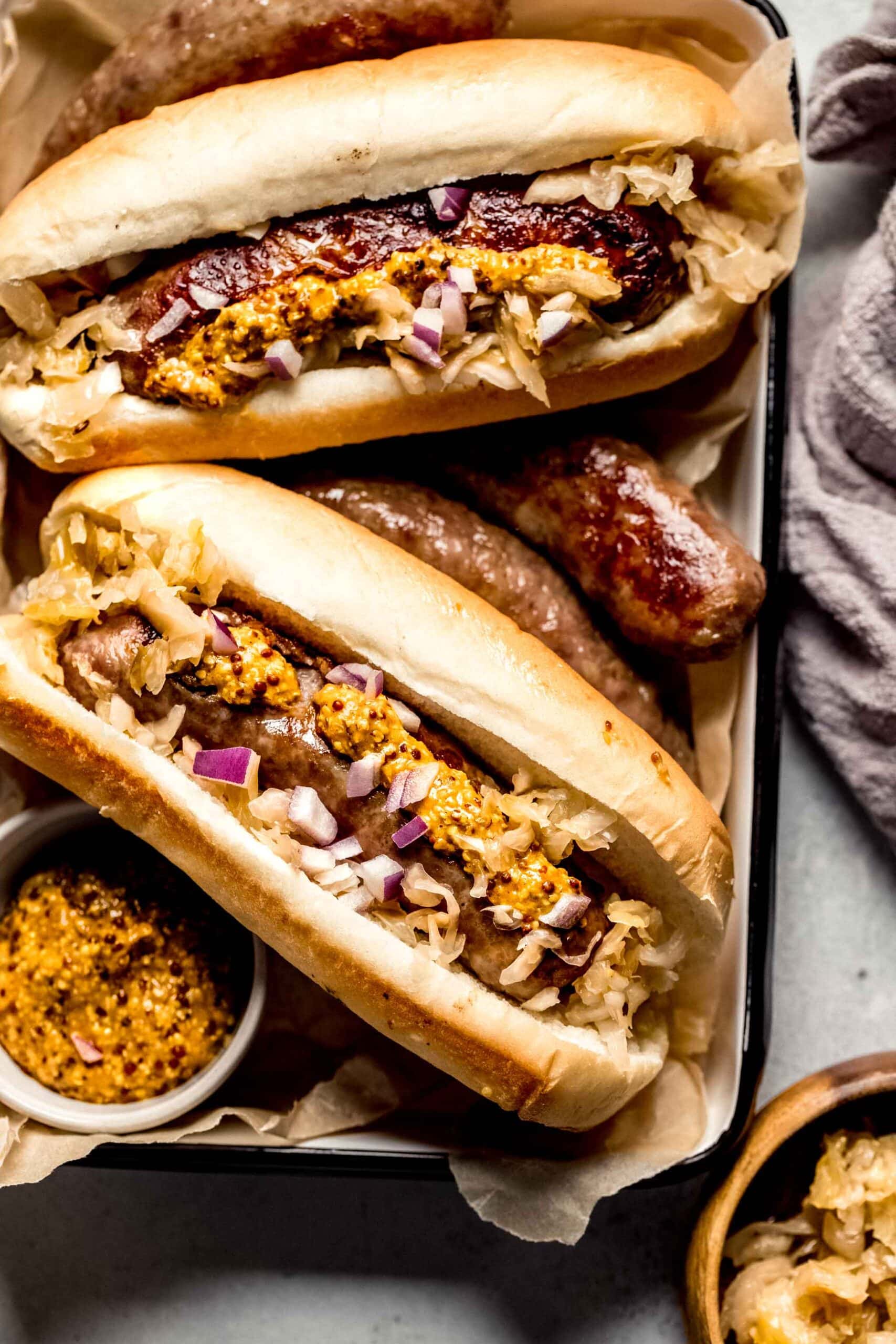 Sausages on small tray with bowl of mustard topped with sauerkraut.