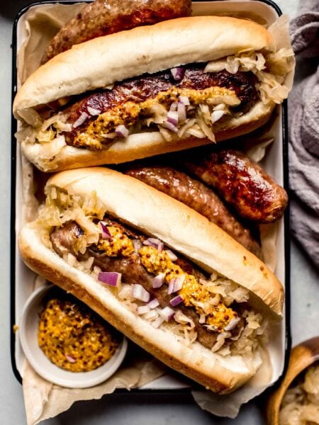 Air fryer brats in buns topped with mustard and red onions.