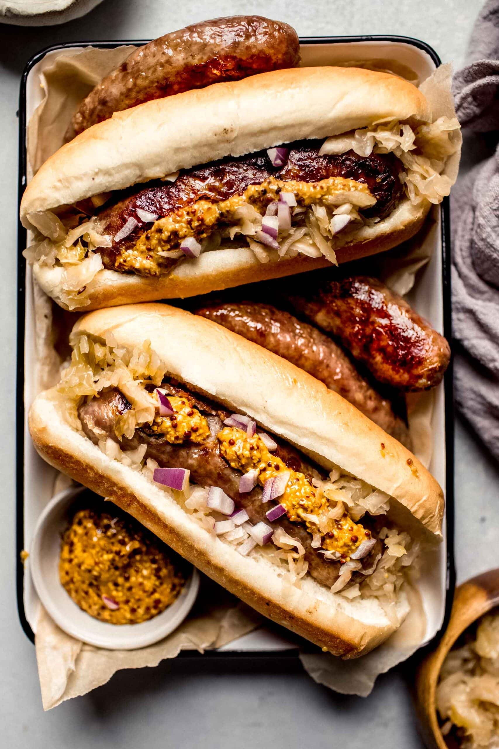 Air fryer brats in buns topped with mustard and red onions.