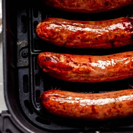 Cooked bratwurst in air fryer basket.