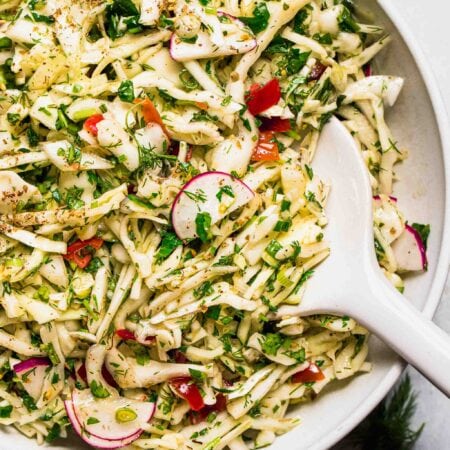 Lebanese cabbage salad in bowl with white serving spoon.
