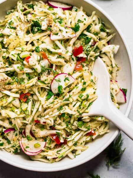Lebanese cabbage salad in bowl with white serving spoon.