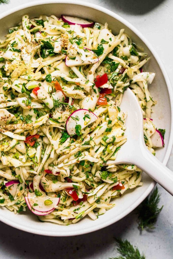 Lebanese cabbage salad in bowl with white serving spoon.