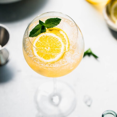 Limoncello spritz garnished with mint sprig and lemon slice in wine glass.
