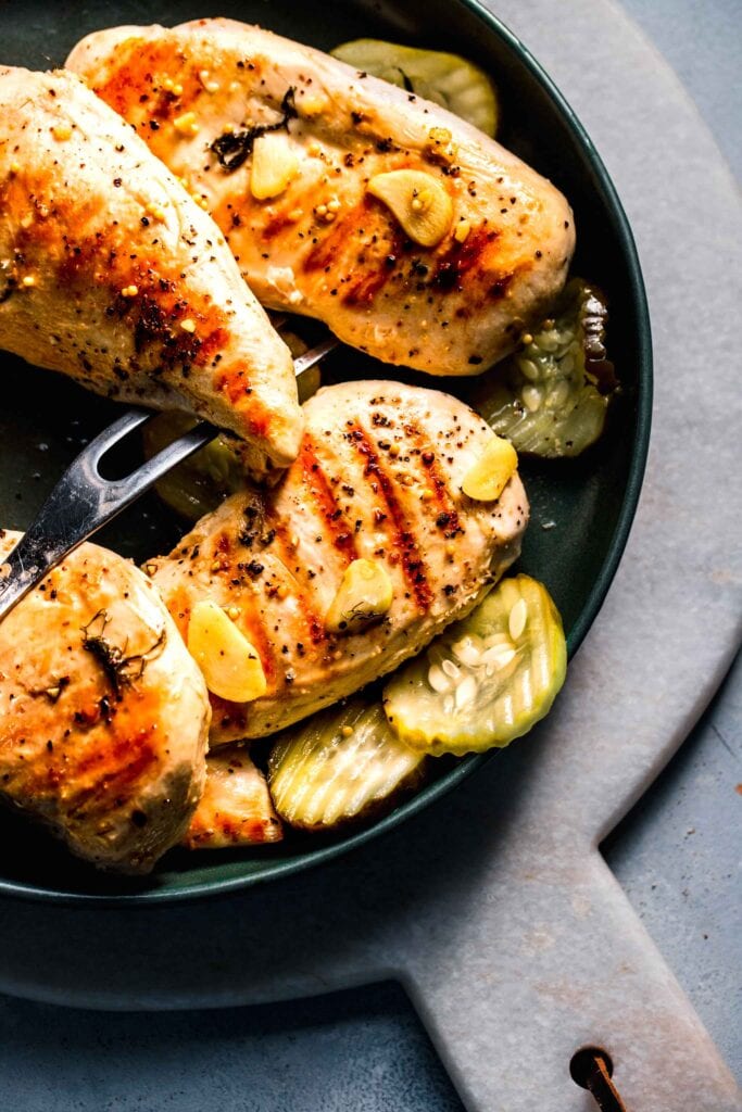 Grilled chicken breasts on plate with pickles.