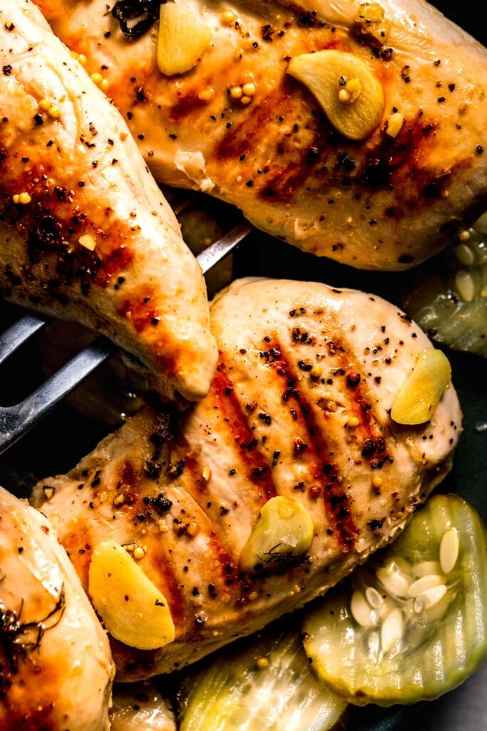 Grilled chicken breasts on plate surrounded by pickles.