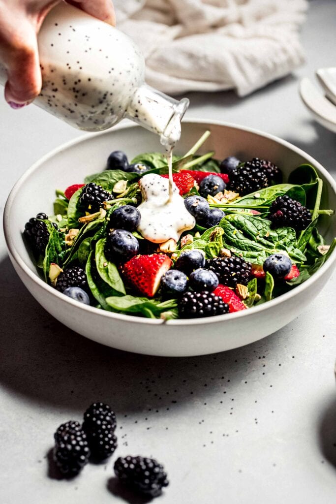 Poppyseed dressing being drizzled on salad. 