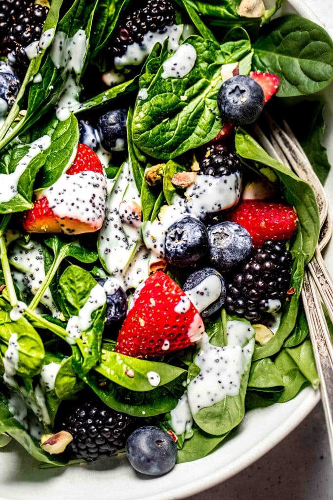 Close up of bowl of spinach salad with berries and poppyseed dressing. 
