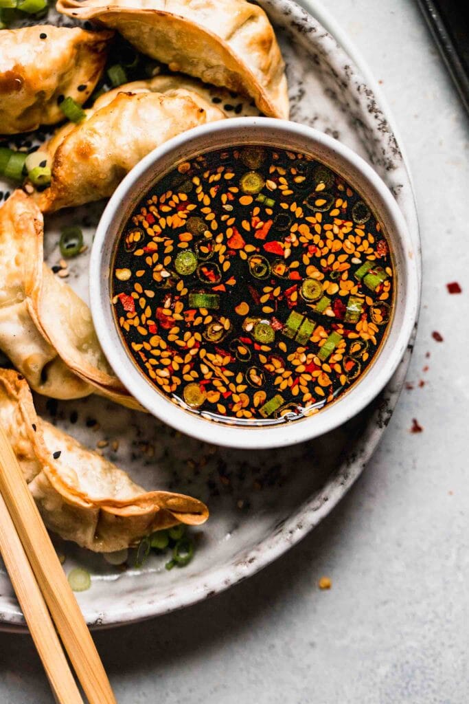 Small bowl of sauce on plate surrounded by potstickers. 