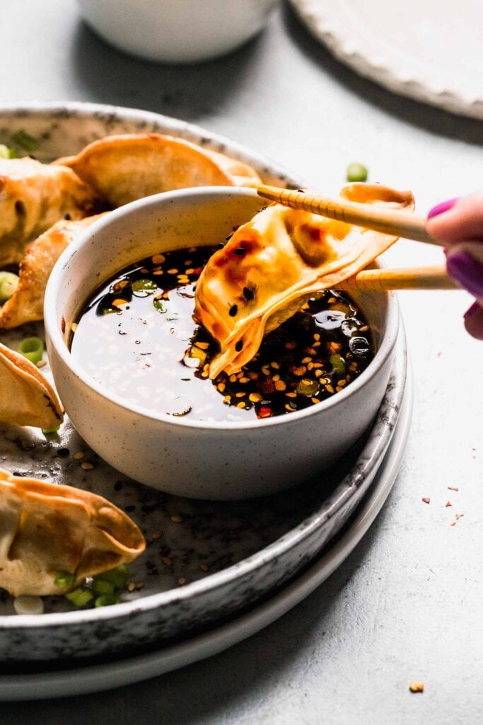 Potsticker being dipped into sauce. 