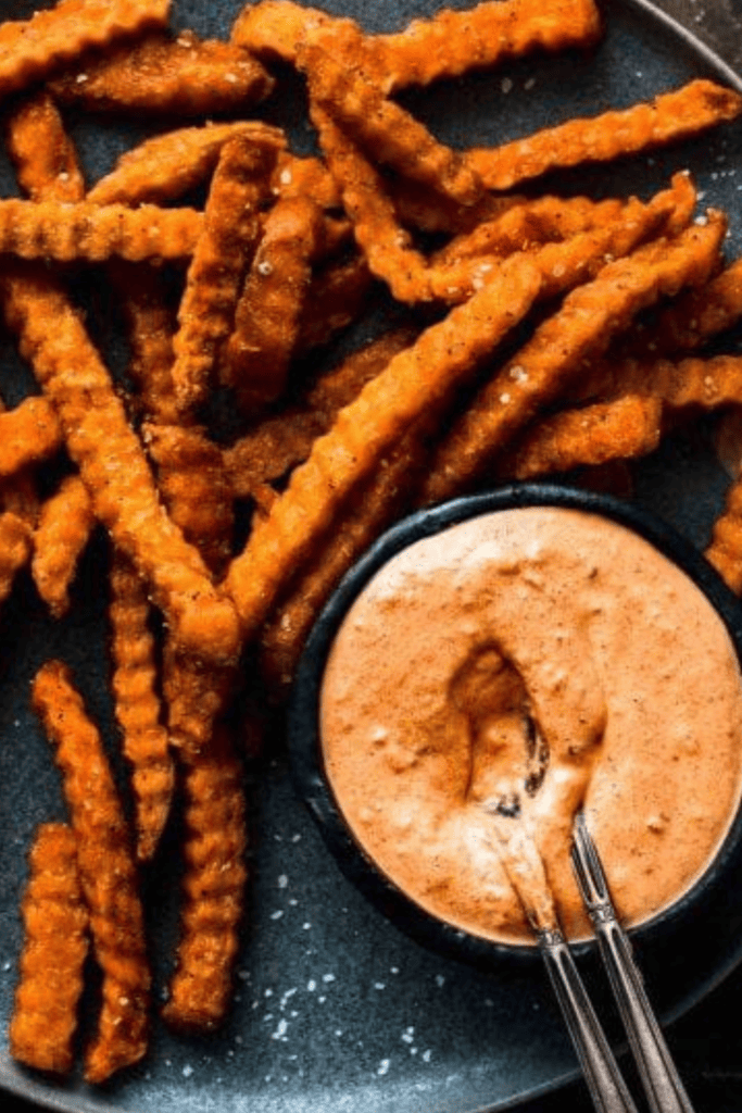 Chipotle crema in small bowl on plate of sweet potato fries.