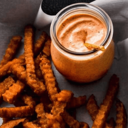 Sauce in small jar on platter of fries.