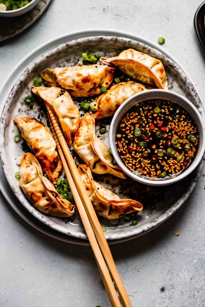 Golden potstickers on plate with bowl of dipping sauce. 